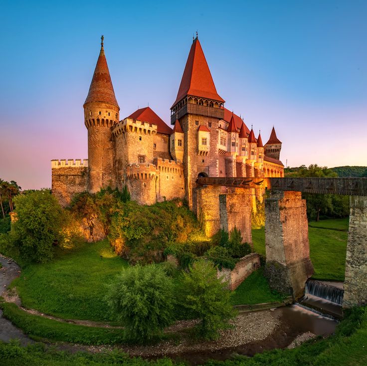 an old castle is lit up in the evening light with its red roof and towers