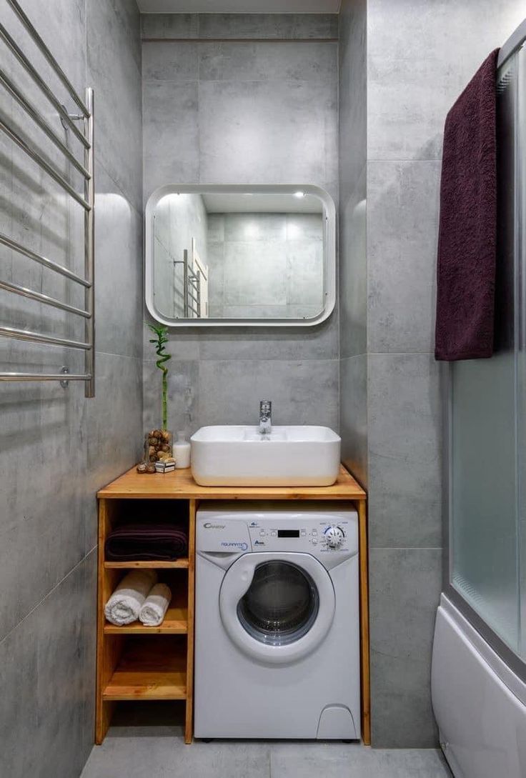 a washer and dryer in a small bathroom with grey tiles on the walls