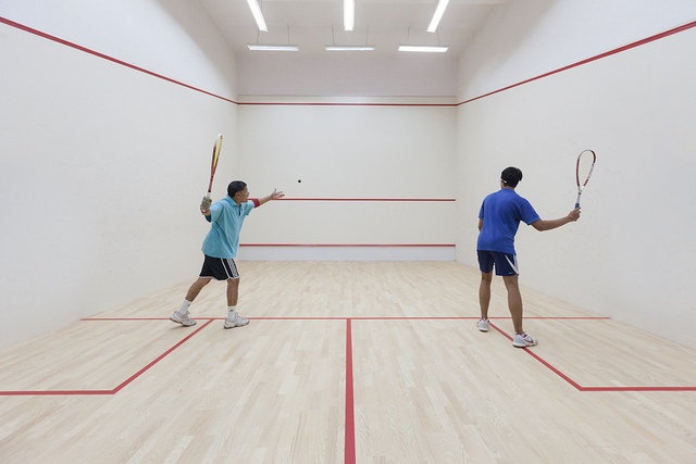 two men playing tennis in an empty room with red lines on the floor and white walls