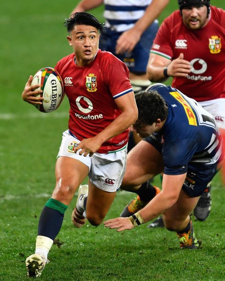 a rugby player running with the ball in his hand and two other players behind him