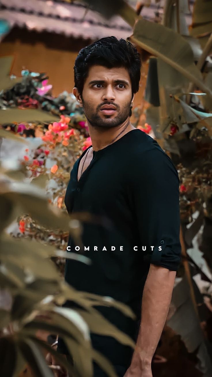 a man is standing in front of some plants and looking at the camera with a serious look on his face