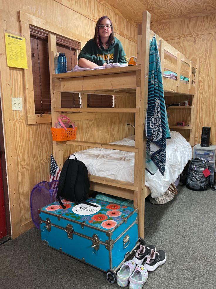 a woman sitting on top of a bunk bed next to a suitcase and other items