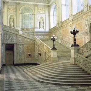 an ornate staircase leading up to the second floor in a building with large windows and chandeliers