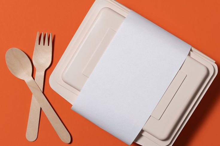 an open box with two forks and a paper napkin on the lid next to it