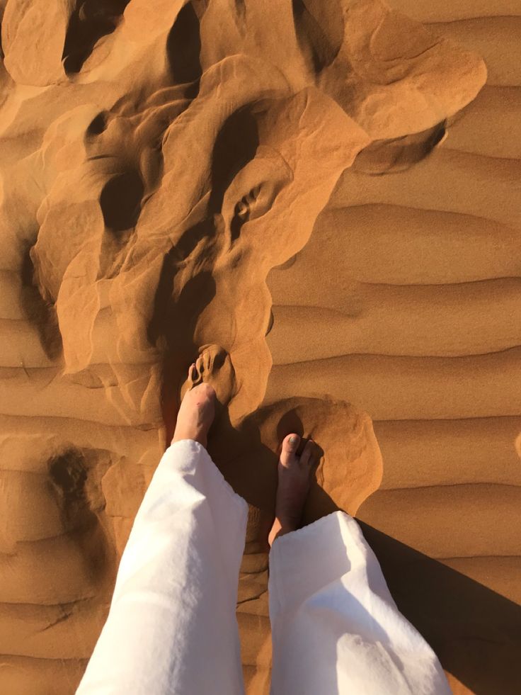 a person standing on top of a sandy beach next to a large rock and sand dune