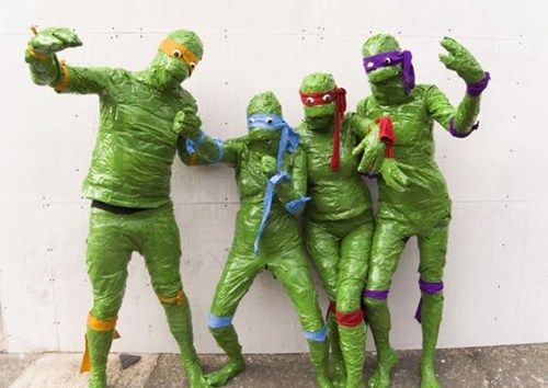 three people in green costumes standing next to each other with their hands up and one person wearing