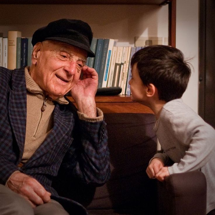 an old man sitting next to a little boy in front of a bookshelf