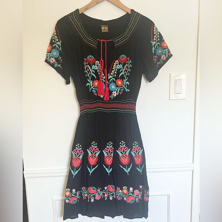 Richie Black Embroidered Dress. Elastic Waist. Floral Design. Tie Neck. Never Worn. In Excellent Condition. Length 38 Elastic Waist 11 Pit To Pit 18 Black Folk Embroidered Summer Dress, Black Folk Style Summer Dress, Black Folk Dress For Spring, Black Bohemian Dress With Floral Embroidery, Bohemian Black Dress With Floral Embroidery, Spring Black Embroidered Dress With Embroidered Hem, Black Fitted Bohemian Embroidered Dress, Fitted Black Bohemian Embroidered Dress, Black Embroidered Dress With Hem Detail For Spring