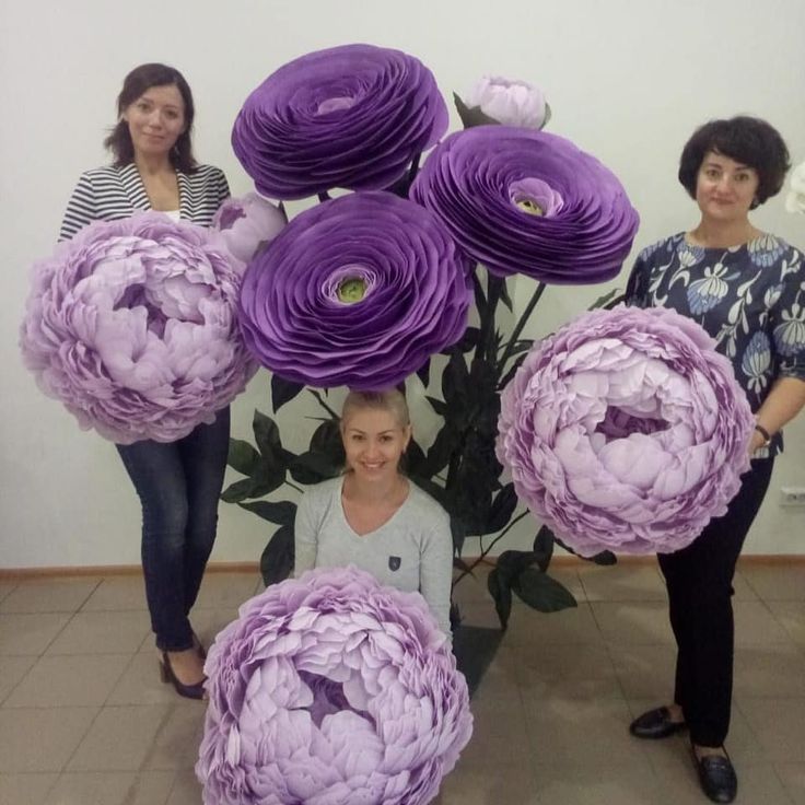 three women standing next to each other holding large purple flowers