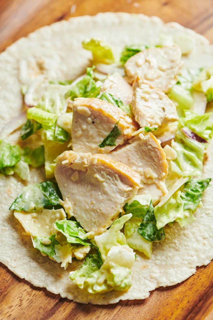 a tortilla topped with chicken and lettuce on top of a wooden table