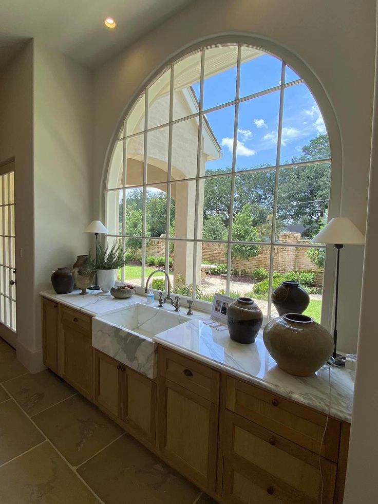 a kitchen with two sinks and large arched window overlooking the garden area in front of it