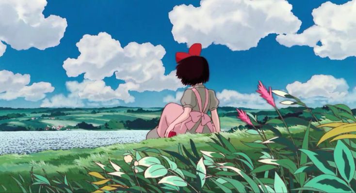 a person sitting on the grass looking at some flowers and clouds in the sky above them