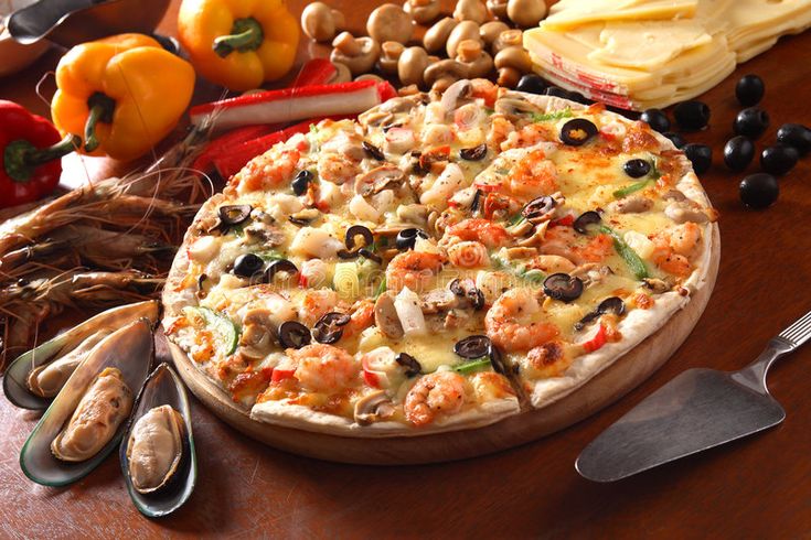 a pizza sitting on top of a wooden table next to vegetables and utensils