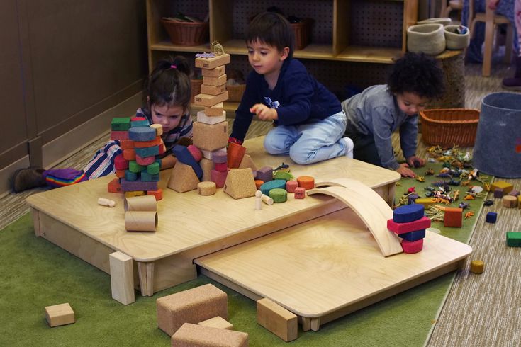 three children playing with wooden blocks in a playroom