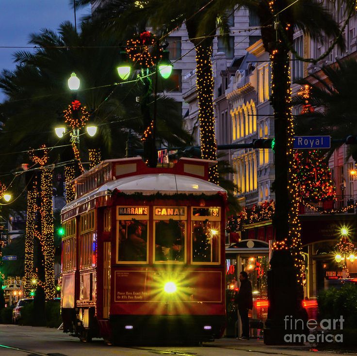 a trolley car driving down the street at night with christmas lights on it's sides