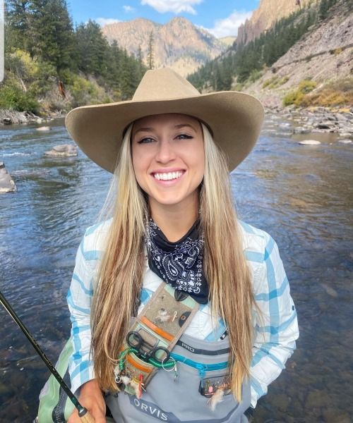 a woman wearing a cowboy hat and holding a fishing rod in the middle of a river