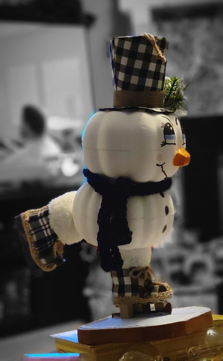 a snowman made out of plastic sitting on top of a wooden table in front of a black and white background