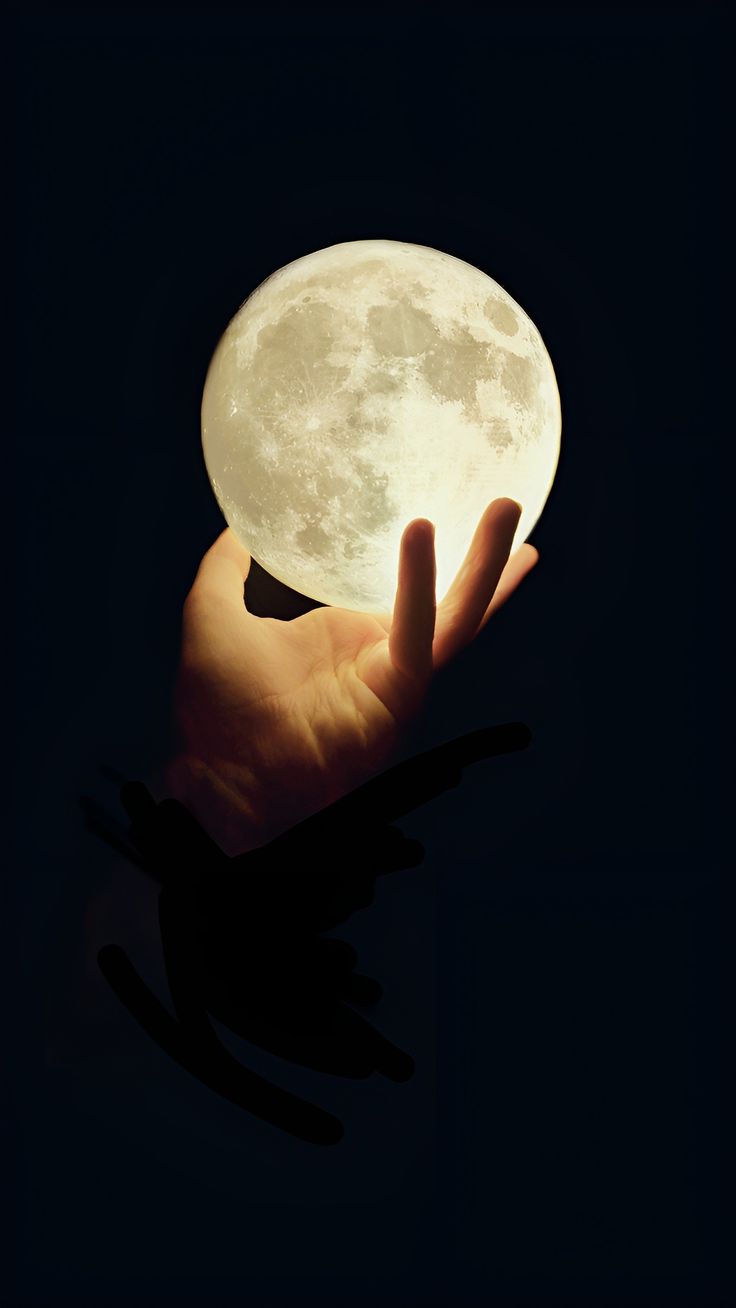 a person's hand holding a lit up moon in the dark