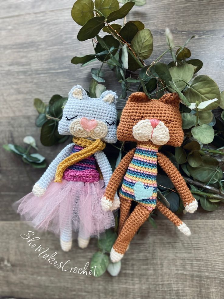 two crocheted cats sitting next to each other on top of a wooden table