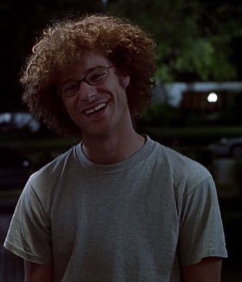 a man with curly hair and glasses smiling