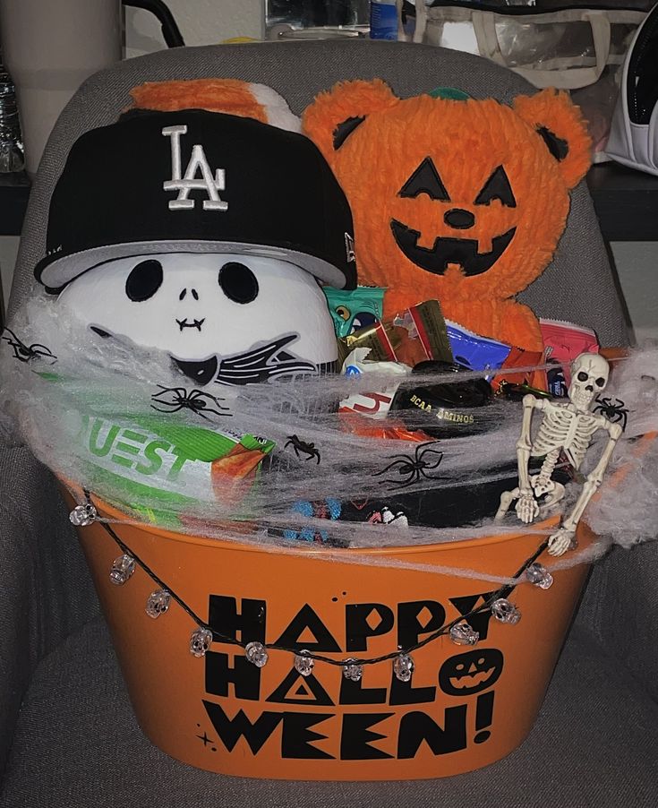 an orange bucket filled with halloween items on top of a gray chair next to a teddy bear