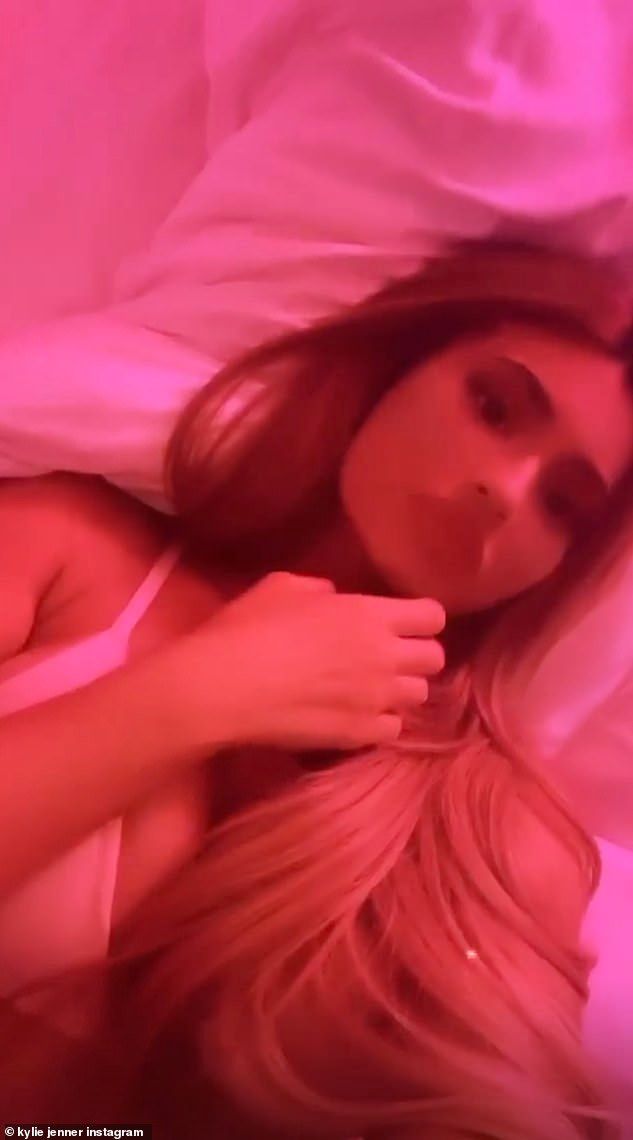 a woman laying in bed under a pink light