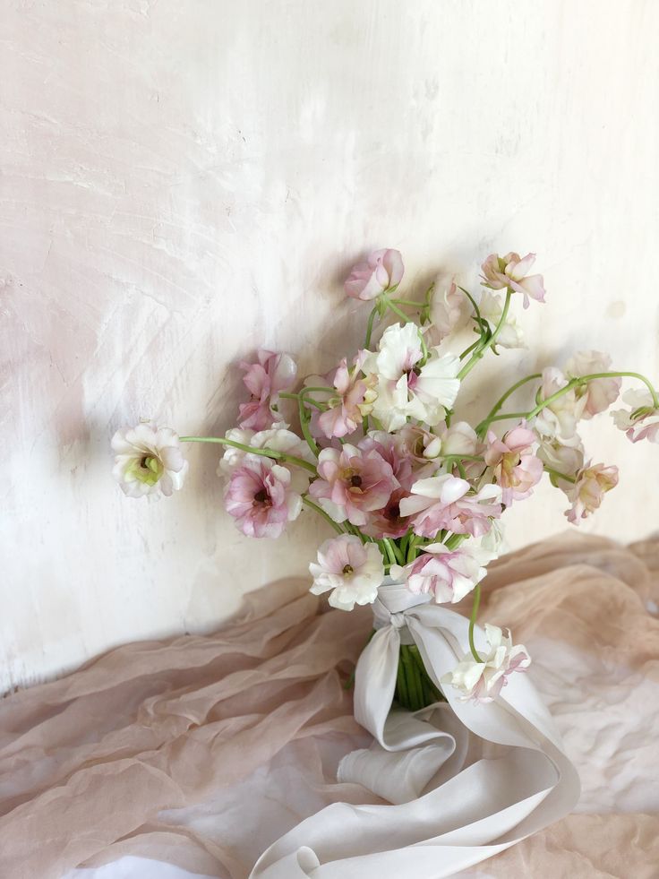 a vase filled with pink and white flowers on top of a bed covered in sheets