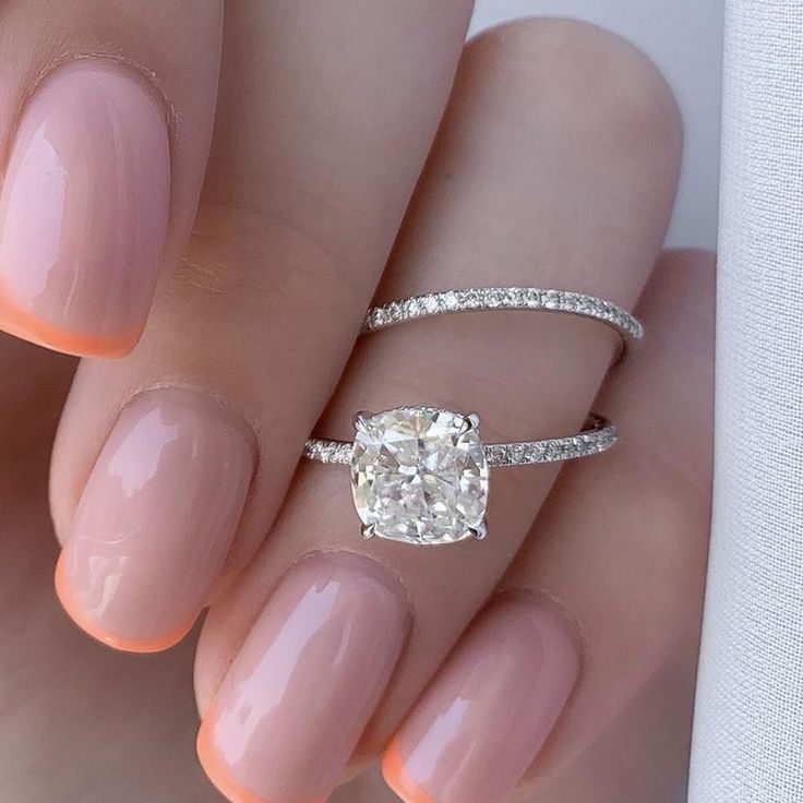 a woman's hand with a ring and a diamond on her left hand, holding a white manicure