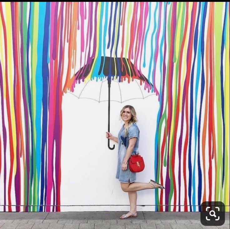 a woman standing in front of a colorful wall with an umbrella and handbag on it