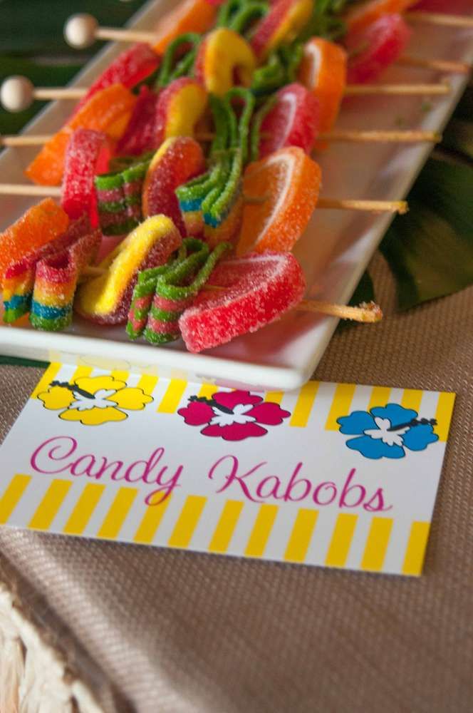 candy kabobs are arranged on a white plate with a yellow striped tablecloth