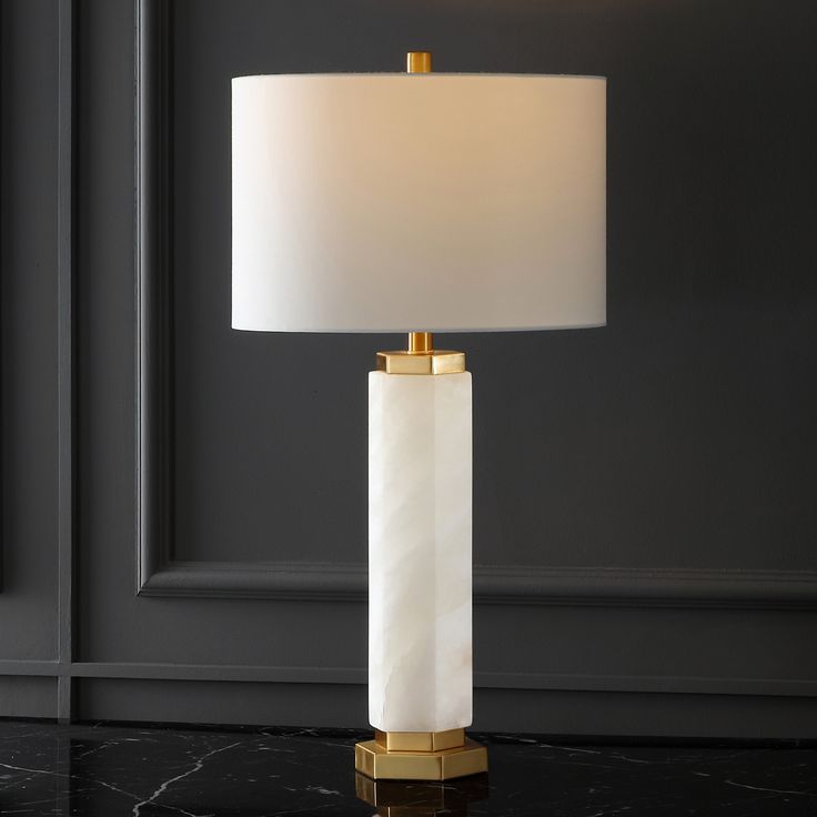 a table lamp with a white shade on the base and a gold trim around it