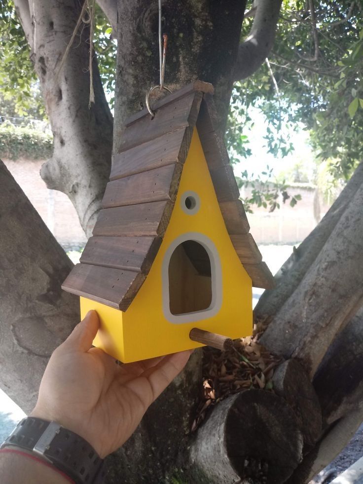 a person holding up a yellow birdhouse in a tree