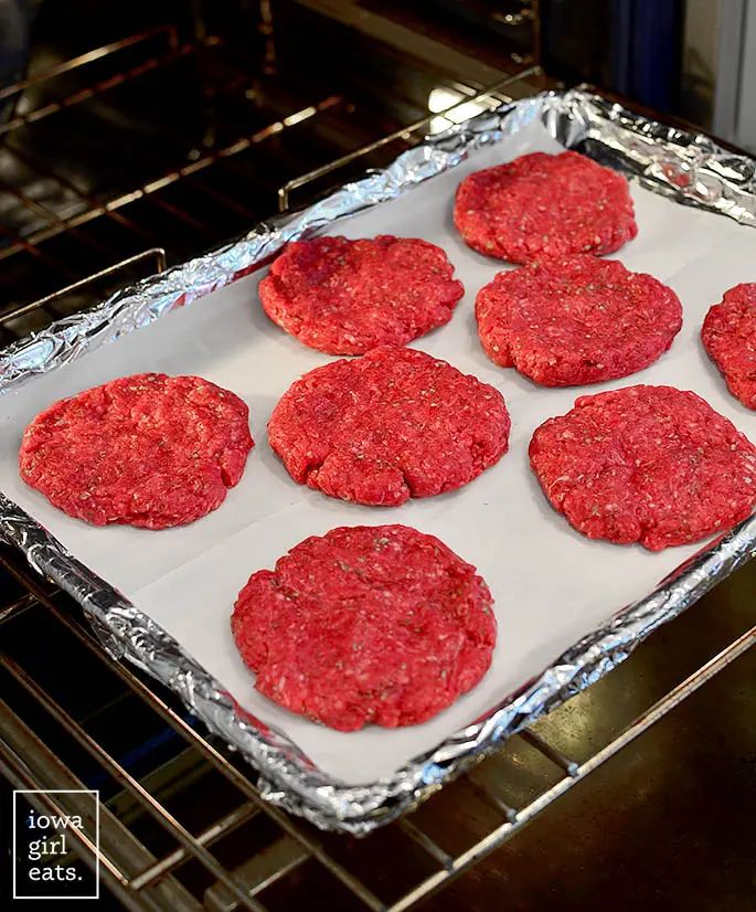 raw hamburger patties on a baking sheet in an oven, ready to go into the oven