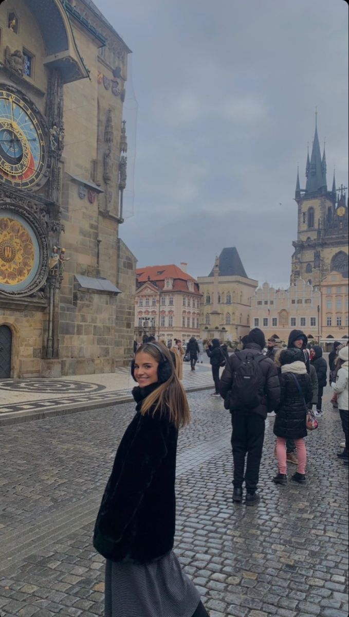 a woman standing on a cobblestone street in front of an old clock tower