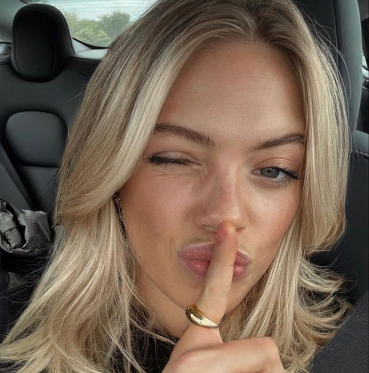 a blonde woman with her finger in her mouth while sitting in the back seat of a car