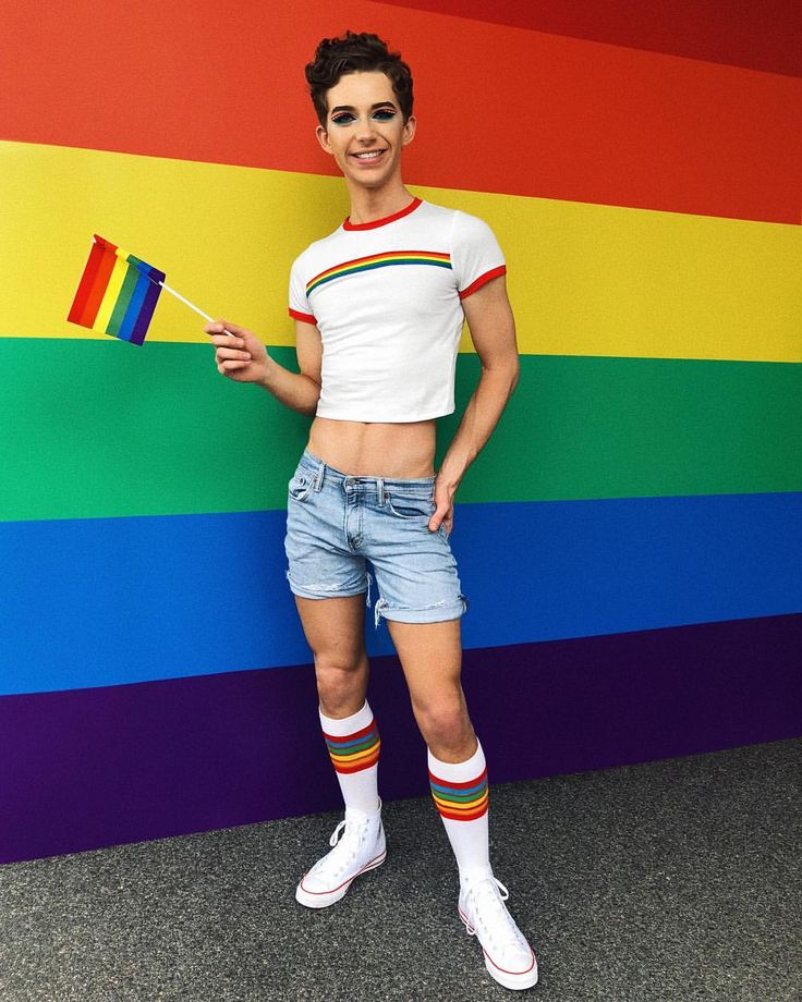 a man standing in front of a rainbow colored wall holding a flag and wearing shorts