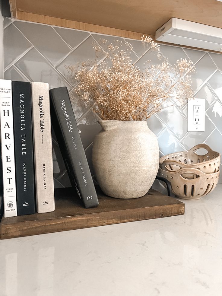 some books are sitting on a shelf next to a vase with dried flowers in it