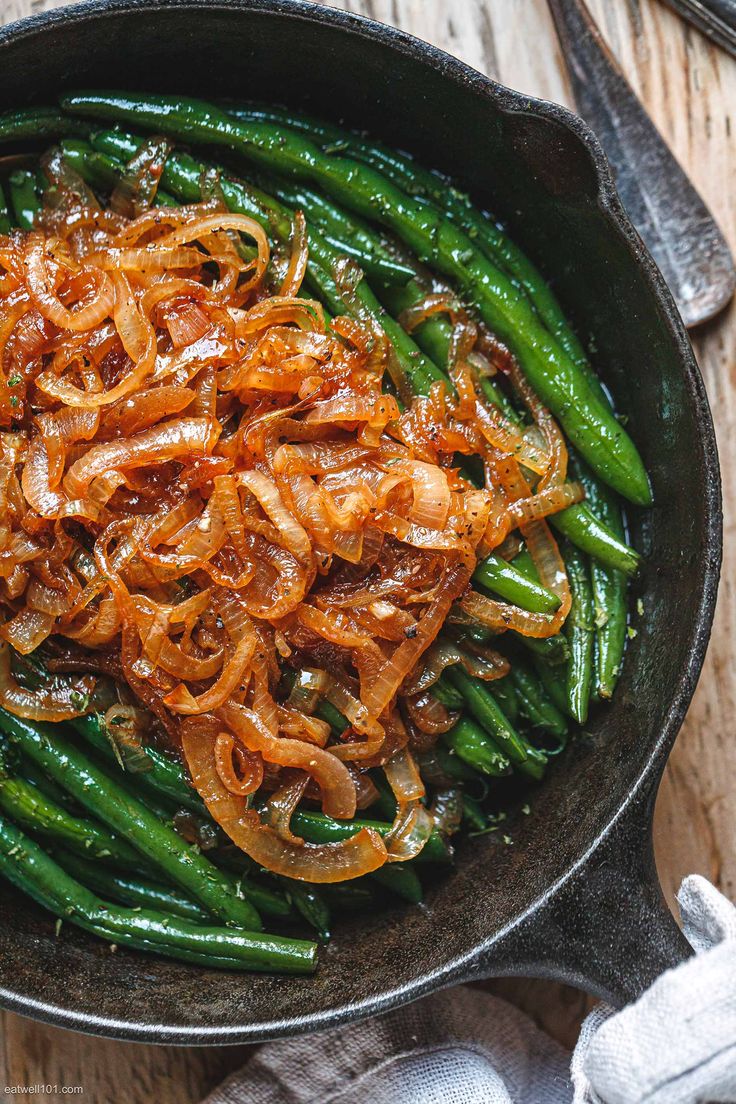 green beans and onions in a frying pan on a wooden table with silverware