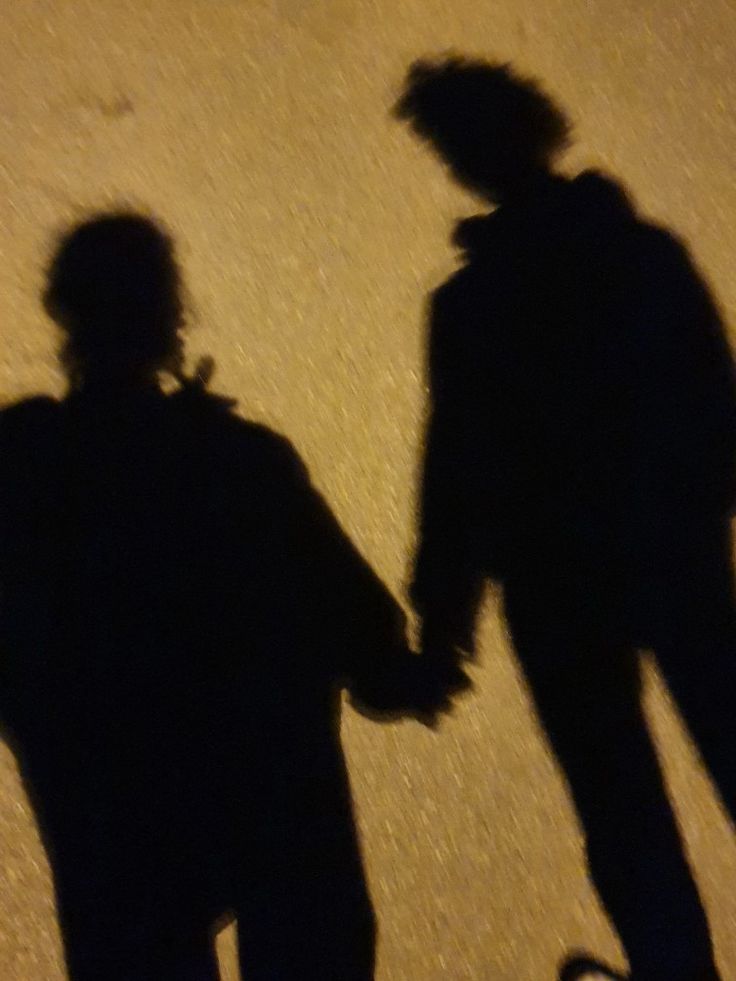 two people standing next to each other with their shadows on the ground and one person holding hands