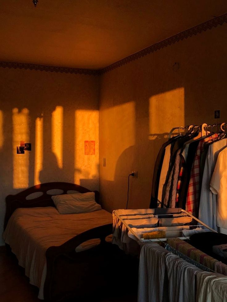 the sun is shining on some clothes hanging in a room with an unmade bed