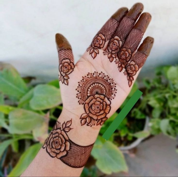 a woman's hand with henna tattoos on it and some plants in the background