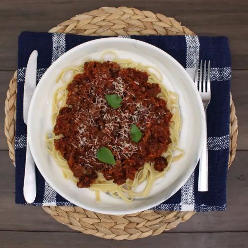 a white plate topped with spaghetti and sauce on top of a blue checkered table cloth