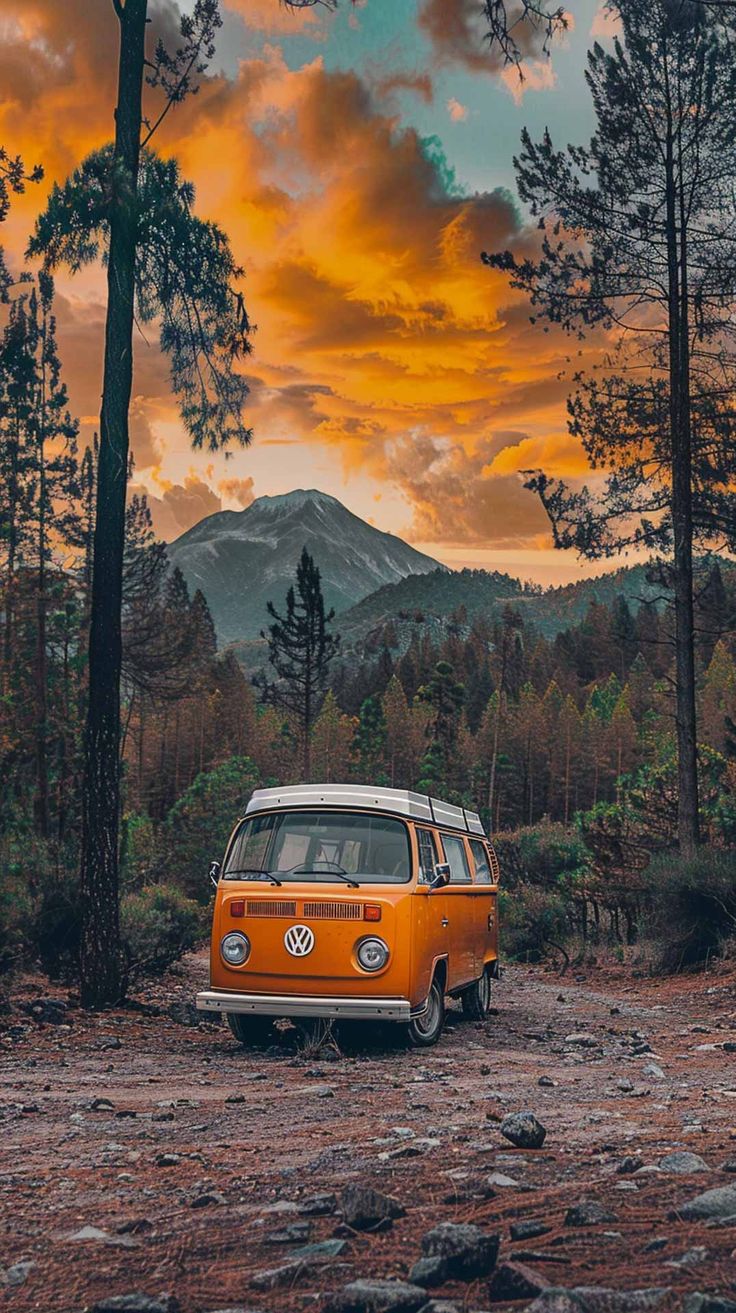 an orange van parked in the middle of a forest with mountains in the back ground