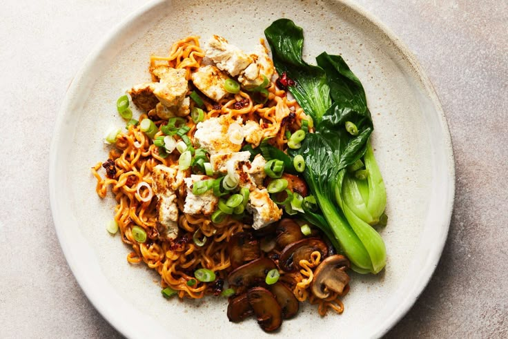 a white plate topped with noodles and veggies on top of a marble table