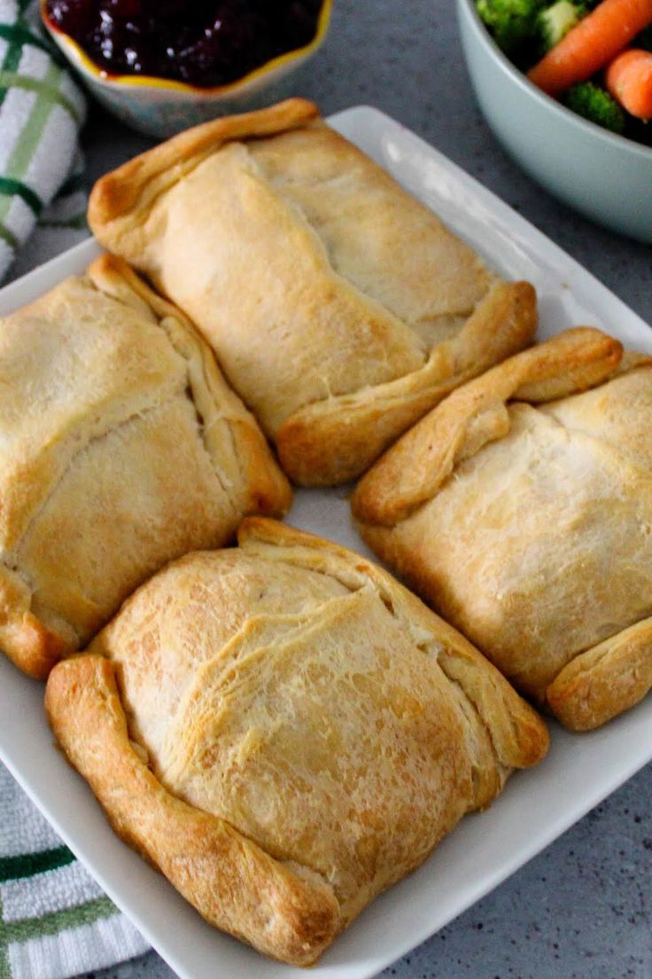 four pastries on a white plate next to a bowl of vegetables