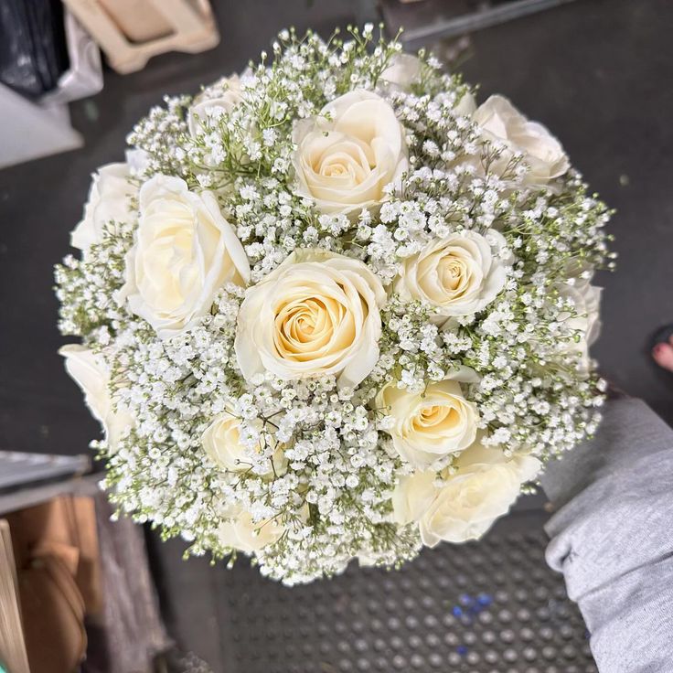 a bouquet of white roses in someone's hand with other flowers on the table