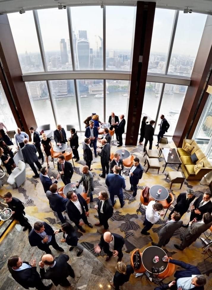 a large group of people standing around in a room with high ceilings and floor to ceiling windows