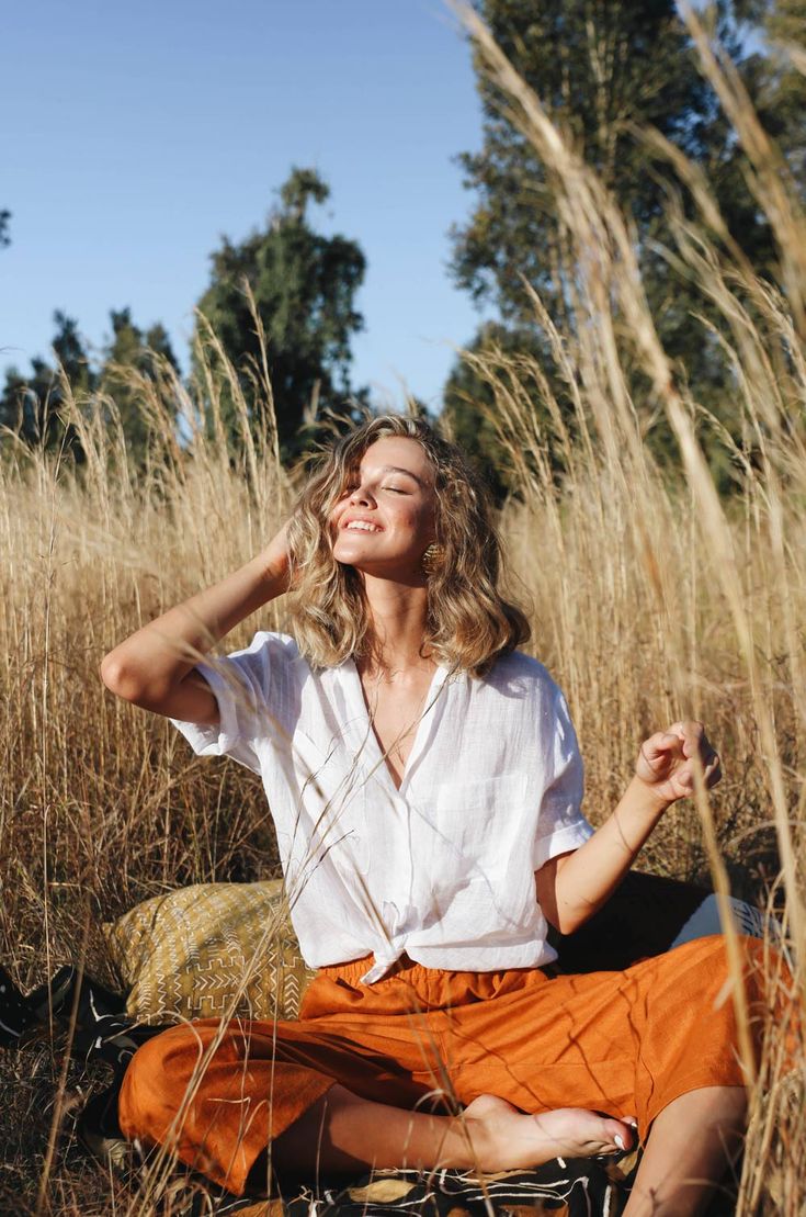 a woman sitting in the middle of a field with her hands on her head and eyes closed