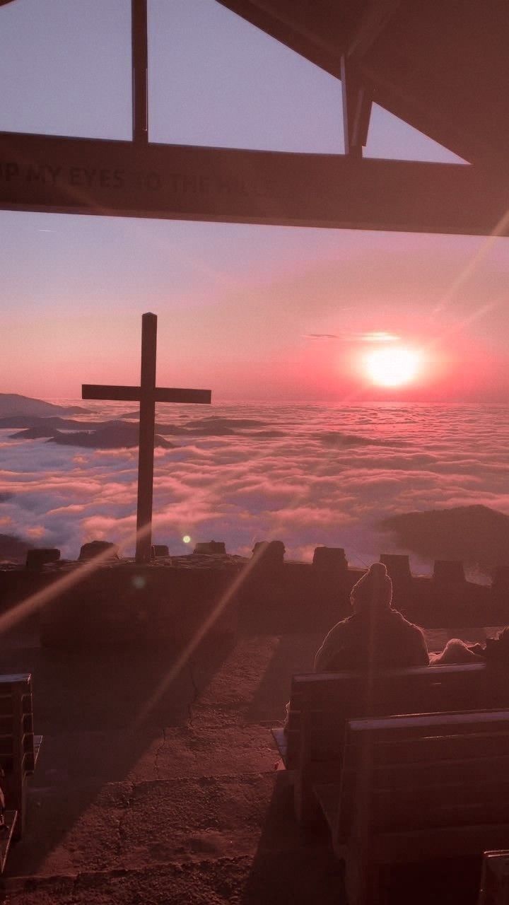 two people sitting on benches at the top of a hill with a cross in the background