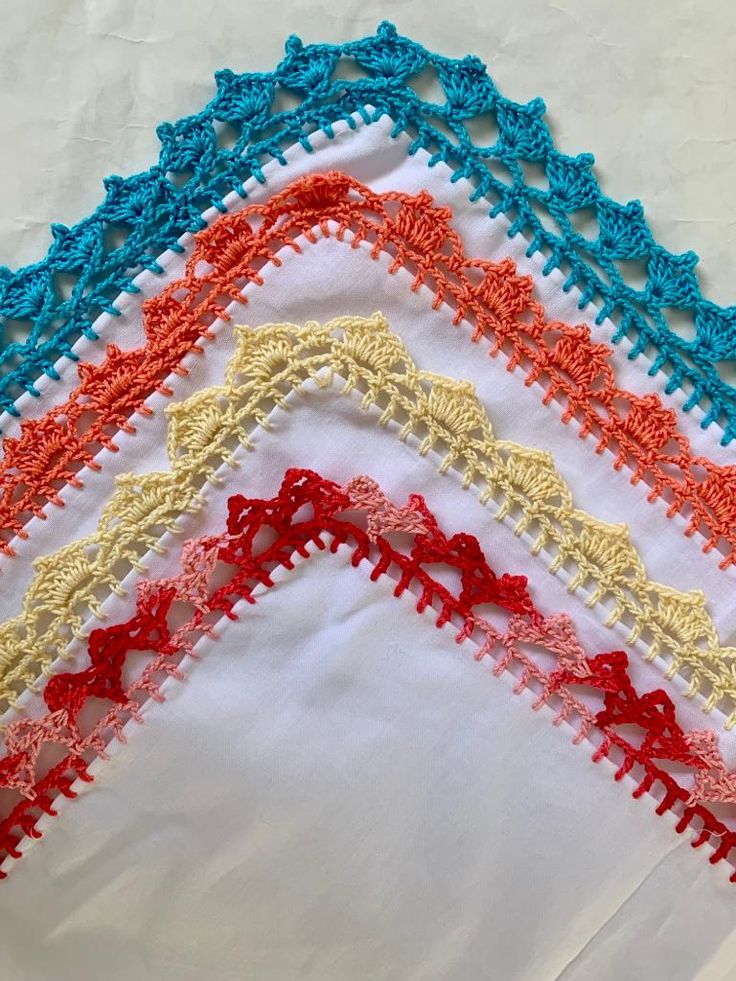 four different colored crochet designs on a white cloth with red, yellow and blue trim